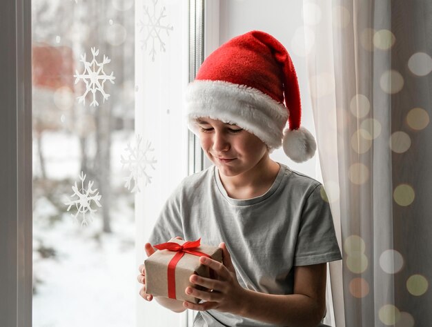 Ein Junge mit Weihnachtsmütze schaut glücklich auf ein Geschenk in seinen Händen.