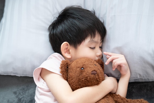 Ein Junge schläft und umarmt einen Teddybären im Bett