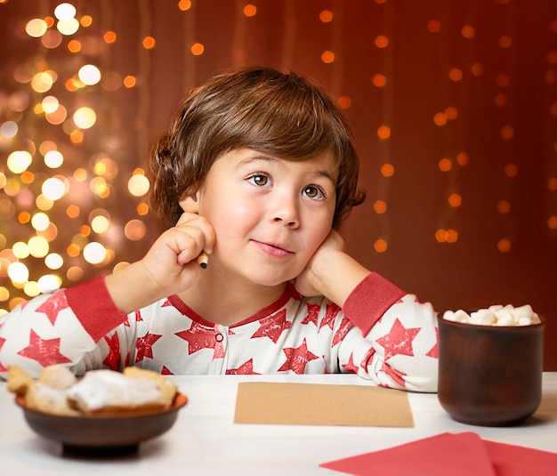 Ein Junge sitzt an einem Tisch vor dem Hintergrund eines Weihnachtsbaumes und schreibt einen Brief an den Weihnachtsmann