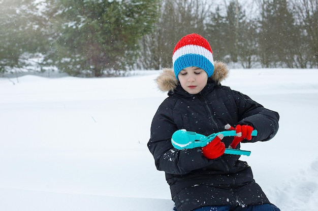 Ein Junge sitzt im Schnee und formt Schneebälle mit einem hellblauen Plastikmodellierwerkzeug