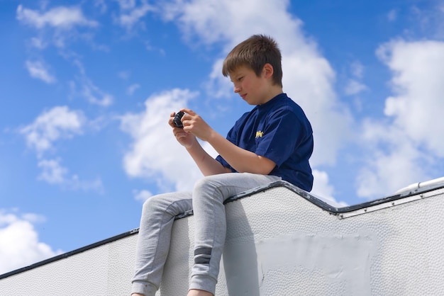 Ein Junge sitzt unter einem wunderschönen blauen Himmel auf dem Dach eines Lieferwagens und macht Fotos