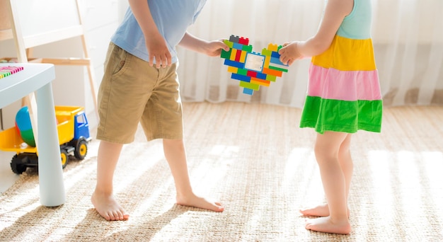 Ein Junge und ein Mädchen halten ein Herz aus Plastikblöcken. Bruder und Schwester haben Spaß beim gemeinsamen Spielen im Zimmer