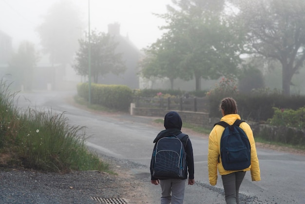 Ein Junge und ein Mädchen im Alter von 8 Jahren mit einem Rucksack gehen im Frühling morgens allein auf einer Landstraße zur Schule