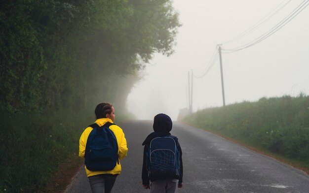 Ein Junge und ein Mädchen im Alter von 8 Jahren mit einem Rucksack gehen im Frühling morgens allein auf einer Landstraße zur Schule