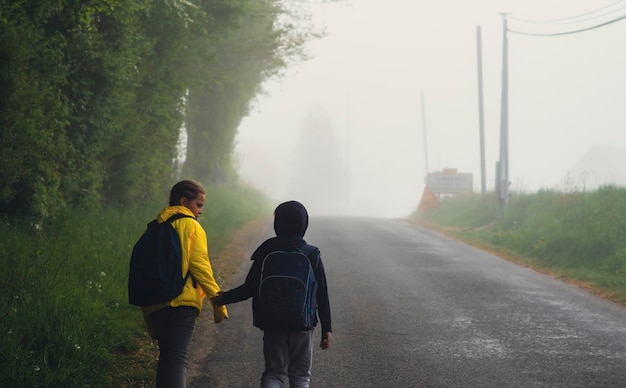 Ein Junge und ein Mädchen im Alter von 8 Jahren mit einem Rucksack gehen im Frühling morgens allein auf einer Landstraße zur Schule