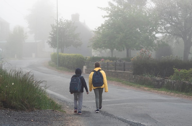 Ein Junge und ein Mädchen im Alter von 8 Jahren mit einem Rucksack gehen im Frühling morgens allein auf einer Landstraße zur Schule