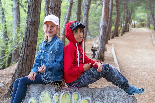 Ein Junge und ein Mädchen sitzen mit dem Rücken zueinander auf einem Felsen in einem Kiefernwald