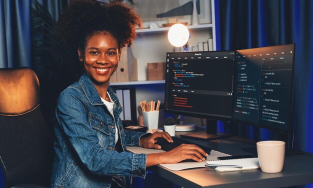 Ein junger afrikanischer IT-Entwickler in Jeans-Hemd präsentiert ein Programm auf einem Computerbildschirm, das codierte Daten von Anwendungen und Websites anzeigt und eine innovative aktualisierte Software-Version Tastemaker erstellt.
