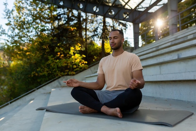 Ein junger Afroamerikaner sitzt im Lotussitz auf einer Matte in einem Stadion und macht Yoga