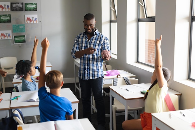 Ein junger afroamerikanischer Lehrer erklärt ein Gehirnmodell für mehrrassige Grundschüler