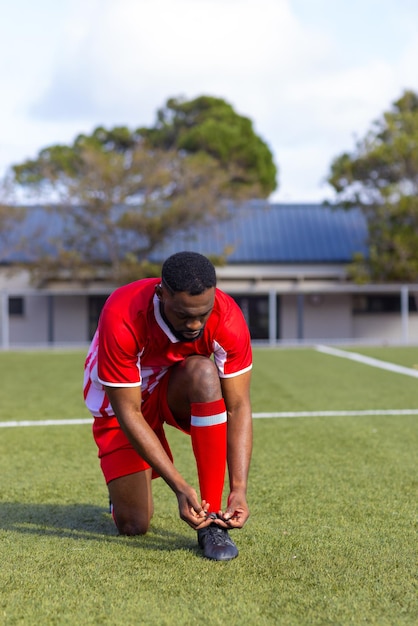 Ein junger afroamerikanischer männlicher Athlet bindet seine Schnürsenkel auf einem Fußballfeld im Freien.