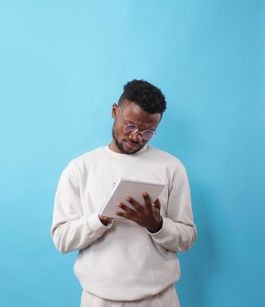 Ein junger afroamerikanischer Mann mit Brille schreibt Informationen in ein Notizbuch auf blauem Hintergrund