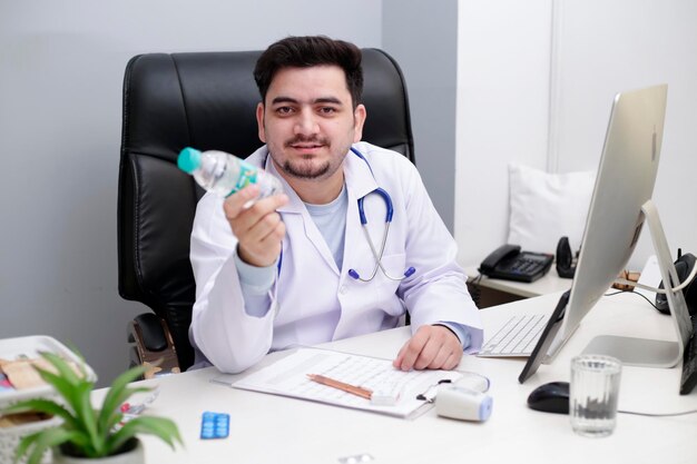 Ein junger Arzt sitzt auf dem Stuhl in der Klinik und gibt eine Wasserflasche