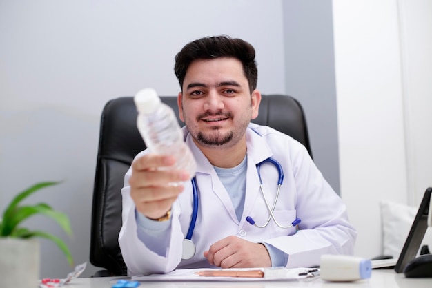 Ein junger Arzt sitzt auf dem Stuhl in der Klinik und gibt eine Wasserflasche