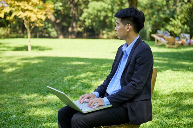 Ein junger asiatischer Geschäftsmann, der im Garten für Arbeit sitzt