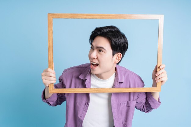 Ein junger asiatischer Mann hält einen Fotorahmen auf blauem Hintergrund