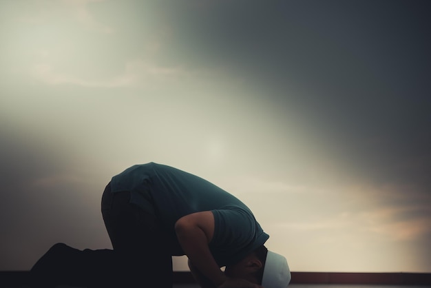 Ein junger asiatischer muslimischer Mann, der auf dem Konzept des SunsetRamadan-Festivals betet