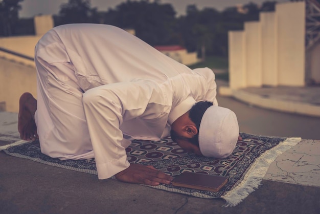 Ein junger asiatischer muslimischer Mann, der auf dem Konzept des SunsetRamadan-Festivals betet