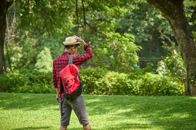 Ein junger asiatischer Rucksacktourist, der eine Kamera hält, die in einem Naturpark steht.