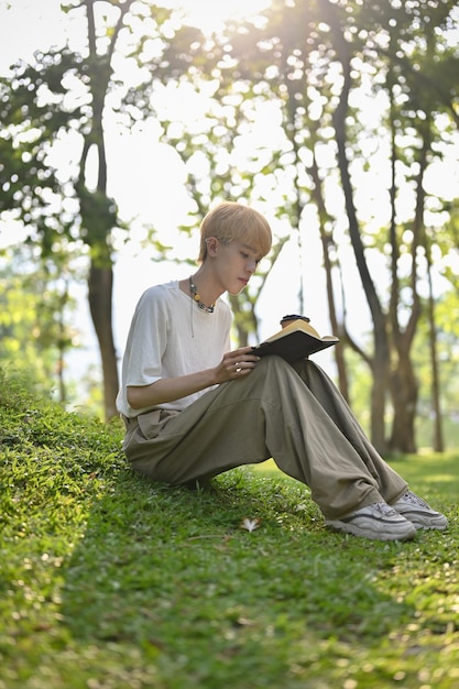 Ein junger asiatischer Schwuler konzentriert sich darauf, ein Buch zu lesen, während er im grünen Park entspannt