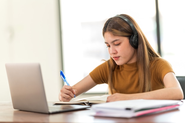 Ein junger asiatischer universitätsstudent, der kopfhörer trägt, um zu hause online zu lernen. während der zeit des virusausbruchs besuchte er keine universität.