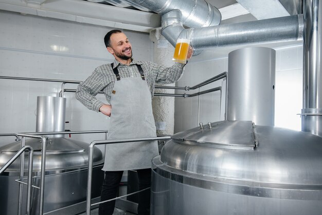 Ein junger bärtiger Brauer führt in der Brauerei die Qualitätskontrolle von frisch gebrautem Bier durch.