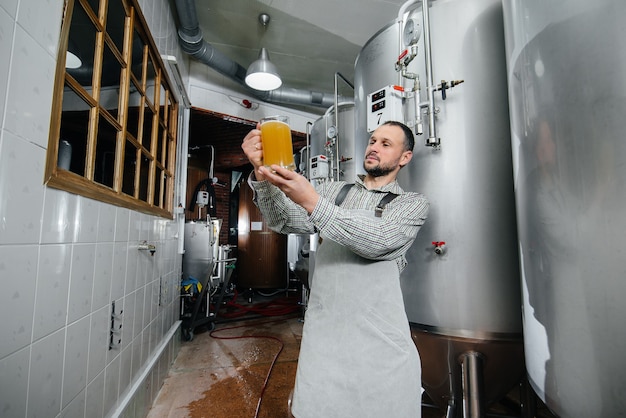 Ein junger bärtiger Brauer führt in der Brauerei die Qualitätskontrolle von frisch gebrautem Bier durch.