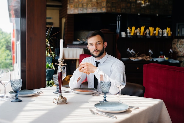 Ein junger bärtiger männlicher Geschäftsmann sitzt an einem Tisch in einem feinen Restaurant und wartet auf seine Bestellung. Kundenservice in der Gastronomie.