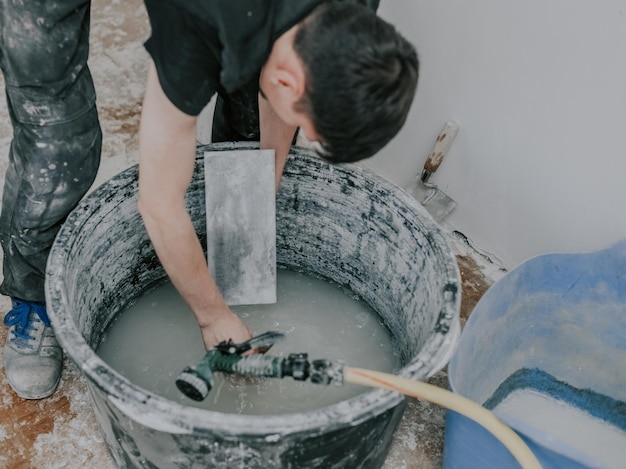 Ein junger Baumeister wäscht Spachtel in einem Becken