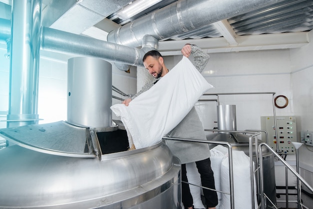 Ein junger Brauer gießt Malz für Bier in einen Behälter. Eine kleine traditionelle Brauerei.