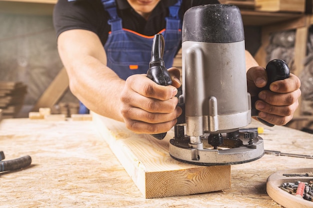 Foto ein junger brünetter zimmermann gleicht einer holzplatte mit einer fräsmaschine in der werkstatt