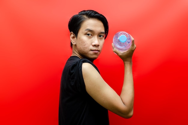 ein junger dünner asiatischer mann, der flaschen wasser wie eine alternative zu hanteln für das heimtraining verwendet