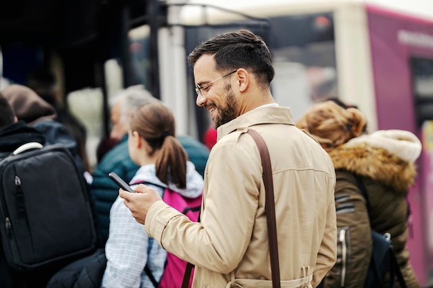 Ein junger, eleganter Geschäftsmann steigt in den öffentlichen Bus ein und lächelt am Telefon, während er Nachrichten schreibt