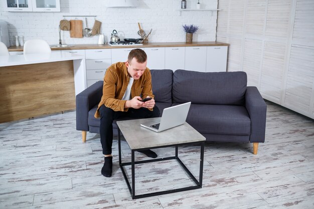 Ein junger erfolgreicher Mann sitzt mit einem Laptop zu Hause auf der Couch und arbeitet. Remote-Arbeit während der Quarantäne.