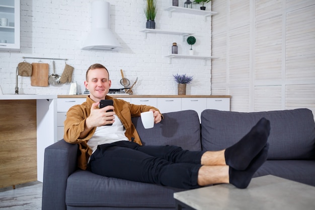 Ein junger erfolgreicher Mann sitzt mit einem Telefon zu Hause auf der Couch und spricht über einen Videolink. Remote-Arbeit während der Quarantäne.