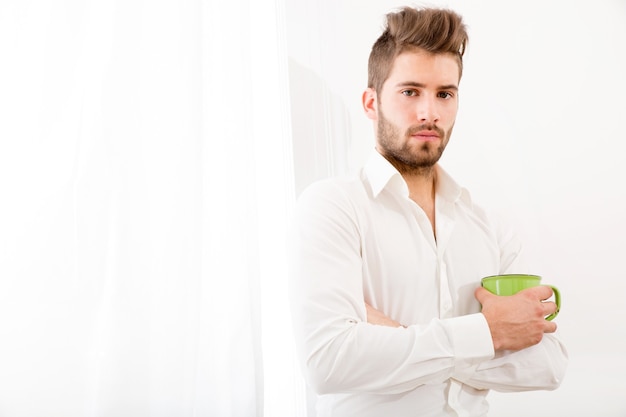 Ein junger erwachsener Mann zu Hause, der Kaffee trinkt.