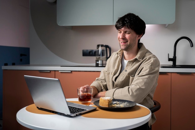 Ein junger freiberuflicher Typ schaut sich einen Film auf einem Laptop an, während er an einem Tisch in der Küche sitzt.