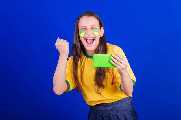 Ein junger Fußballfan aus Brasilien hält ein Handy in der Hand, das ein Spiel anschaut und für Smartphone-Anwendungen jubelt