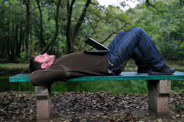 Ein junger Geschäftsmann arbeitet am Laptop im Freien mit grüner Natur im Hintergrund