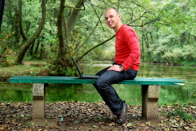 Ein junger Geschäftsmann arbeitet am Laptop im Freien mit grüner Natur im Hintergrund