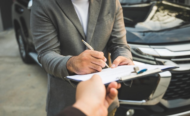 Ein junger Geschäftsmann unterzeichnet einen Luxusauto-Leasingvertrag und einen Autoversicherungskaufvertrag auf den Dokumenten gemäß der Vereinbarung