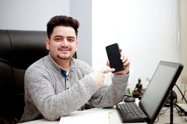 Ein junger Geschäftsmann zeigt Handy und lächelt.