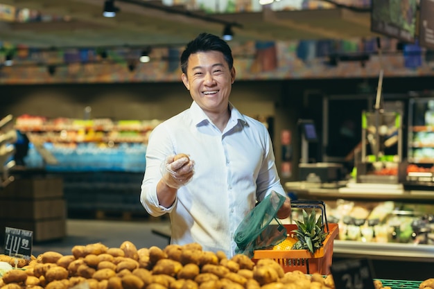 Ein junger gutaussehender asiatischer geschäftsmann steht in einem supermarkt in der gemüseabteilung