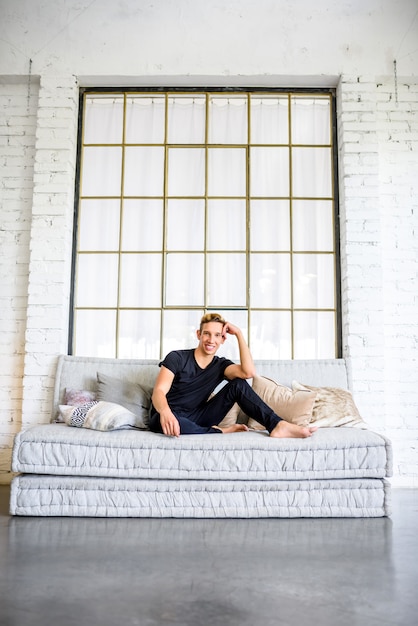 Ein junger gutaussehender Mann, der sich auf dem Sofa in einer Wohnung im Loftstil entspannt