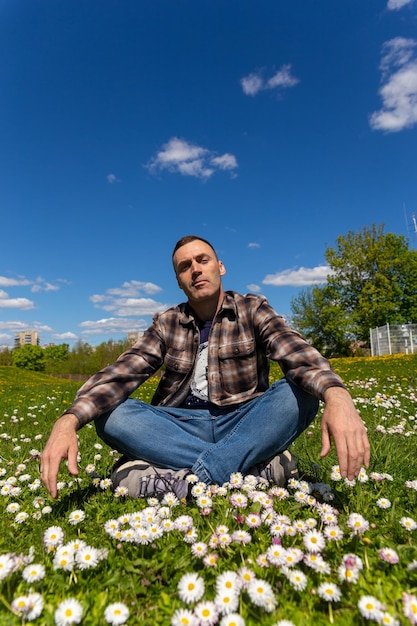 Ein junger, gutaussehender Mann sitzt an einem sonnigen Tag auf einer sonnigen Blumenwiese und amüsiert sich