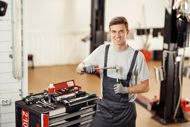 Ein junger gutaussehender Mechaniker ist bei seiner Arbeit und bereitet sich auf die Reparatur eines Autos vor.