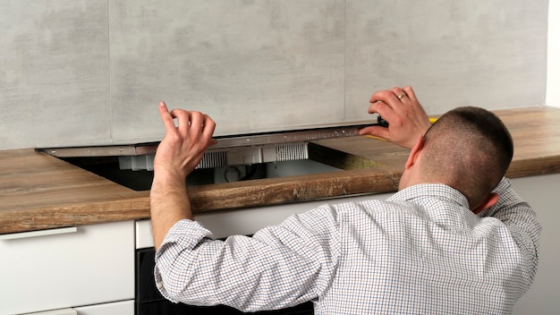 Ein junger Handwerker installiert ein schwarzes Induktionskochfeld in einer modernen weißen Küche im skandinavischen Stil mit einer Betonwand. Elektriker Mann, mach es selbst. Hausarbeiten.