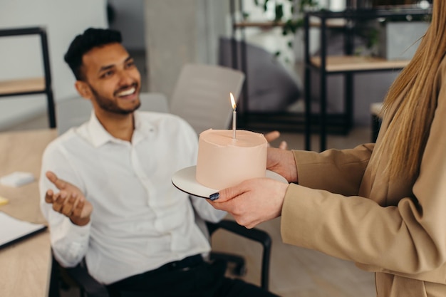 Ein junger Hindu-Mann ist dabei, Kerzen auf einem Kuchen auszublasen und sich während einer Geburtstagsfeier mit Kollegen etwas zu wünschen. Kollegen feiern Geburtstag im Büro