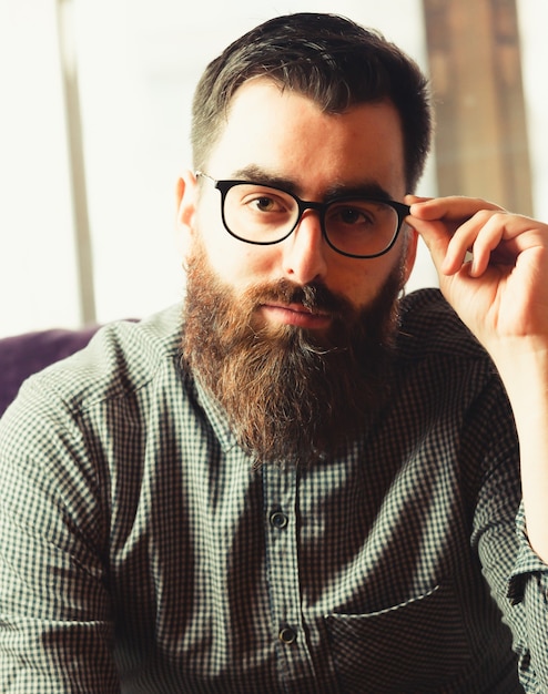 Foto ein junger hipster-mann, der seine blaulichtbrille hält, während er zur kamera mit einem lächelnden gesicht schaut