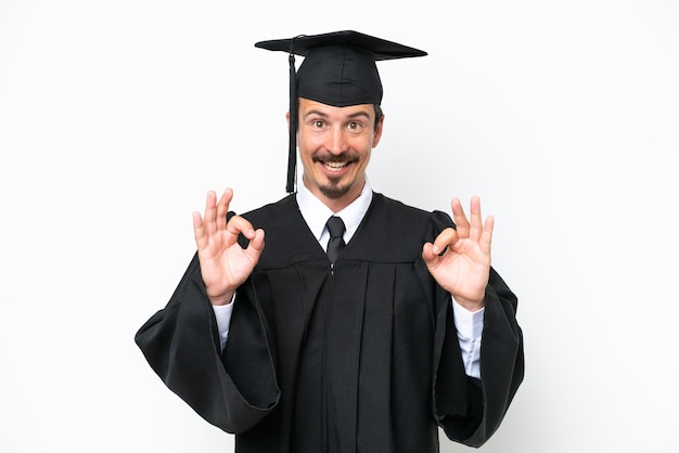 Ein junger Hochschulabsolvent, der auf weißem Hintergrund ein OK-Zeichen mit Fingern zeigt